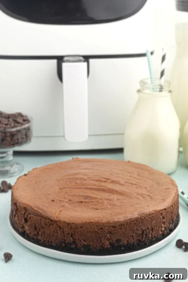 Decadent Air Fryer Chocolate Cheesecake 8 Full chocolate cheesecake, served on a white late, before being sliced, in front of the air fryer.