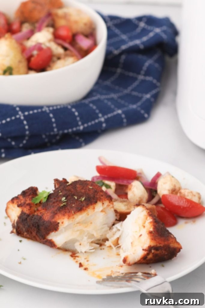 Perfectly Flaky Air Fryer Cod 2 Flaky cod on a white plate seasoned and garnished with tomatoes and other veggies, ready to eat
