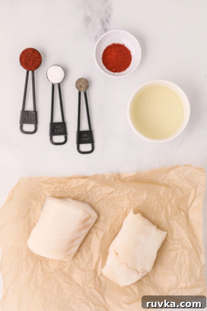 Perfectly Flaky Air Fryer Cod 3 Ingredients needed to make air fryer cod with seasonings measured out and on a white table, including cod fillets, olive oil, and spices