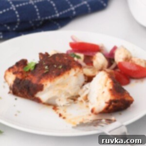 Perfectly Flaky Air Fryer Cod 8 Flaky seasoned cod filet on a white plate garnished with vegetables