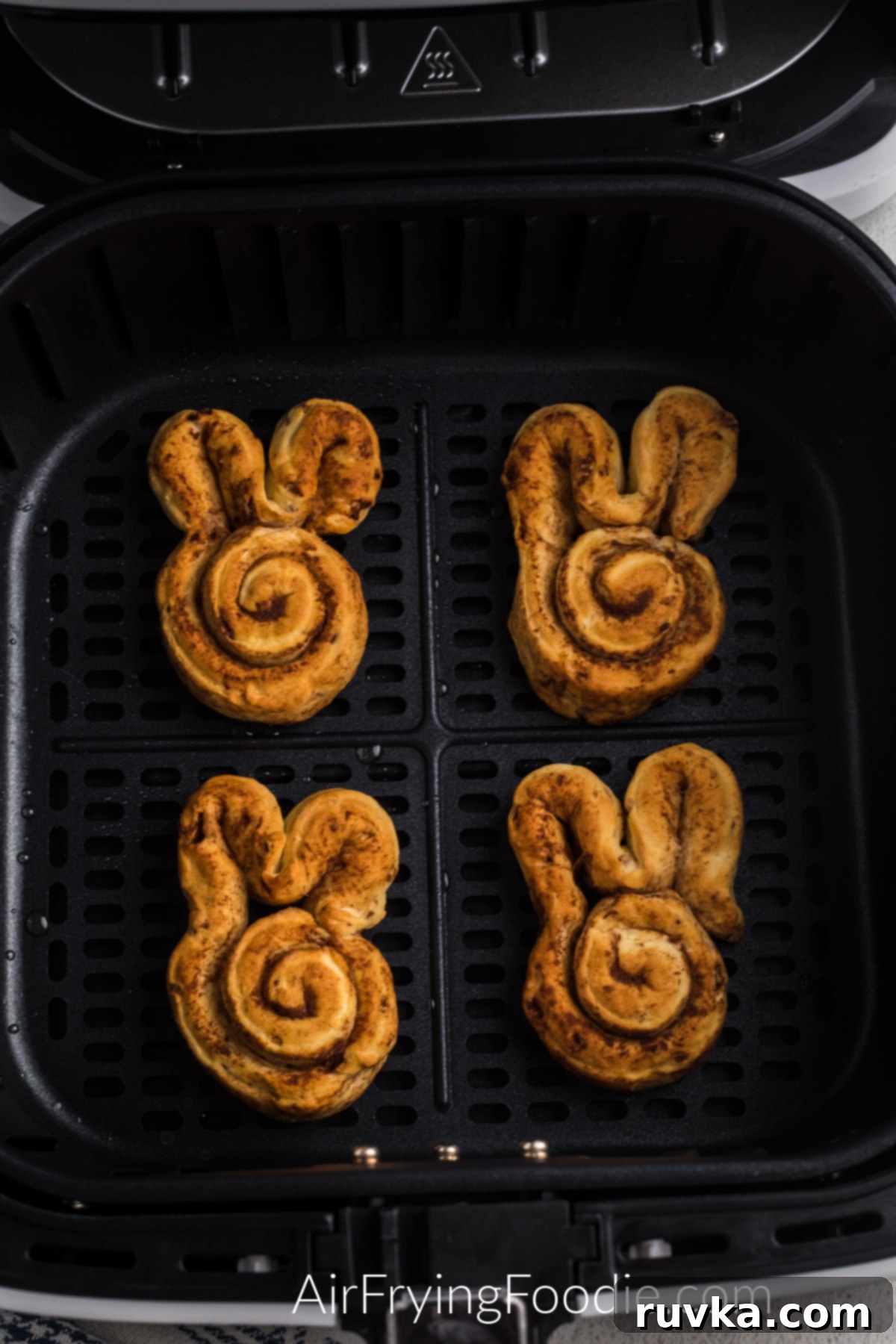 Air Fryer Cinnamon Bunny Delights 5 Air fried cinnamon roll bunnies, perfectly golden brown, nestled in the basket of an air fryer, freshly cooked and ready to be removed.