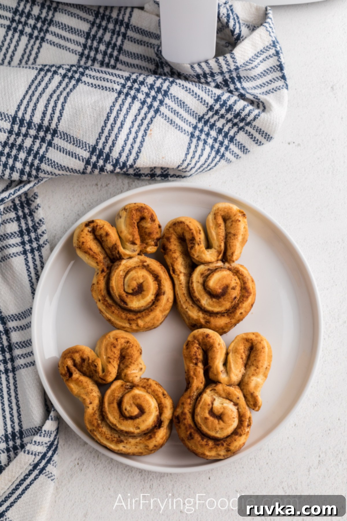 Air Fryer Cinnamon Bunny Delights 6 Freshly air-fried cinnamon roll bunnies, unglazed, arranged neatly on a white plate, showcasing their golden hue and readiness for frosting.