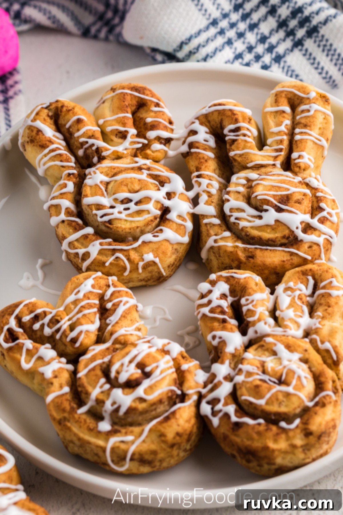 Air Fryer Cinnamon Bunny Delights 7 A delightful arrangement of air-fried cinnamon roll bunnies, generously topped with a sweet, white glaze and served on a simple white plate, ready for an indulgent breakfast.