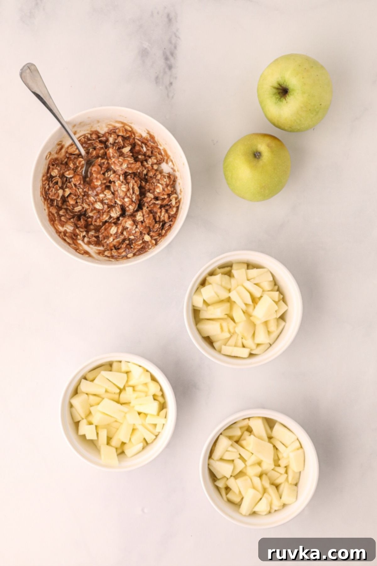 Easy Air Fryer Apple Crisp 4 apples divided into ramekins and oats mixed with spices and sugars in a white bowl