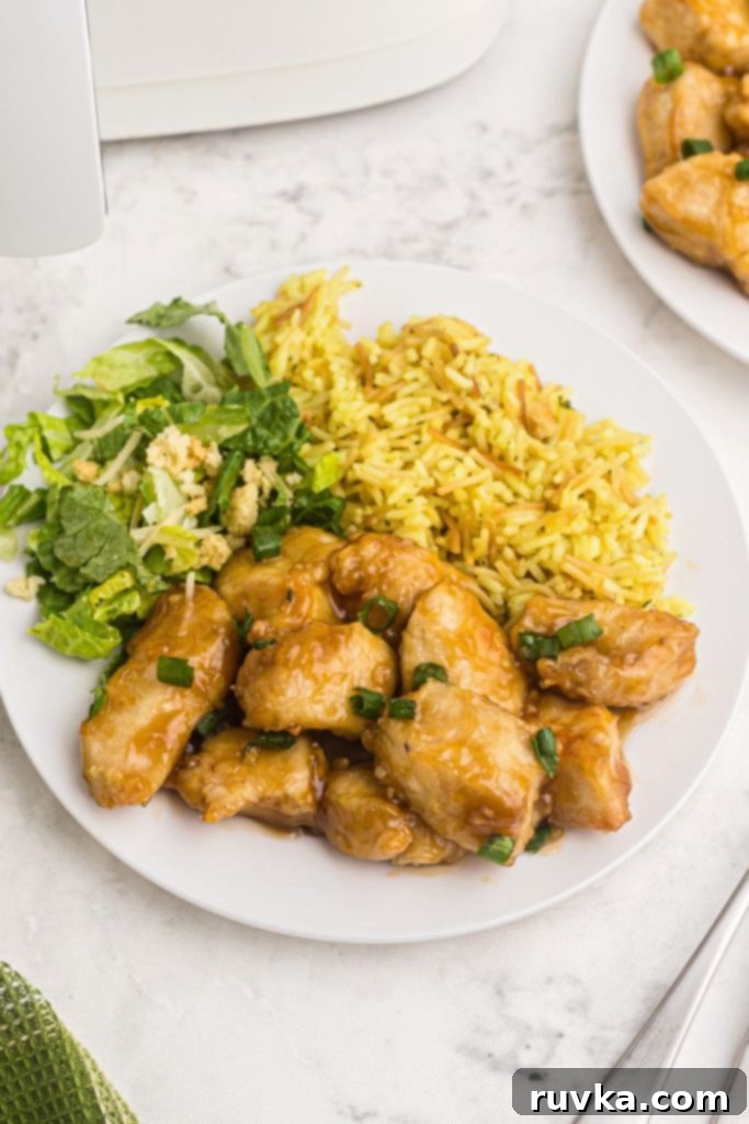 Crispy Air Fryer Sweet & Tangy Chicken 2 Golden crispy chicken on a white plate served with rice and lettuce, tossed in a sweet and sour sauce.