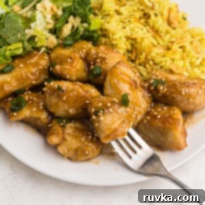 Crispy Air Fryer Sweet & Tangy Chicken 11 Close up fork shot of sweet and sour chicken served on a white plate with rice and salad