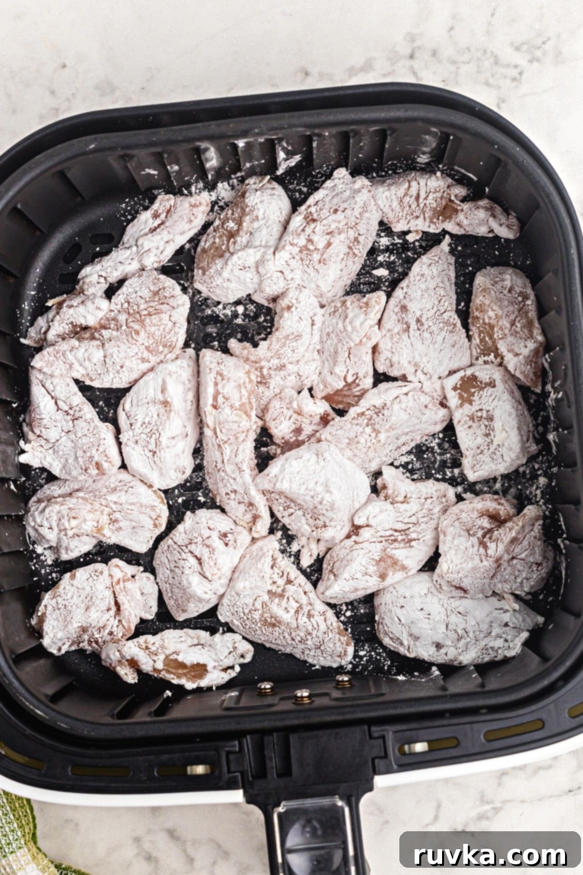 Crispy Air Fryer Sweet & Tangy Chicken 5 chicken coated in cornstarch placed in the air fryer basket.