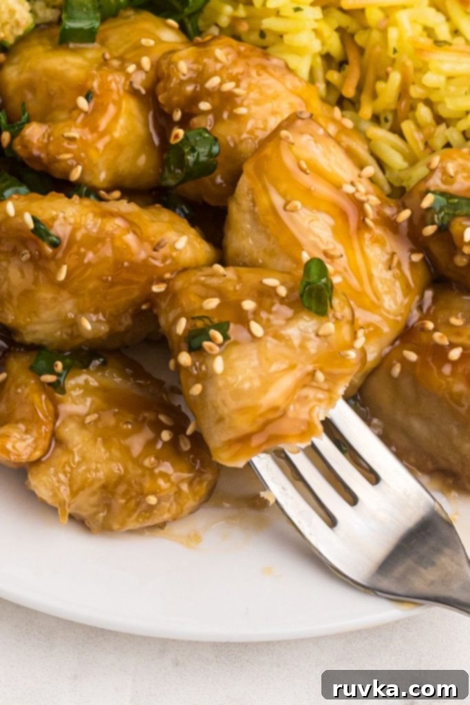 Crispy Air Fryer Sweet & Tangy Chicken 10 Close up bite of sweet and sour chicken on a fork, garnished with sesame seeds and green onions