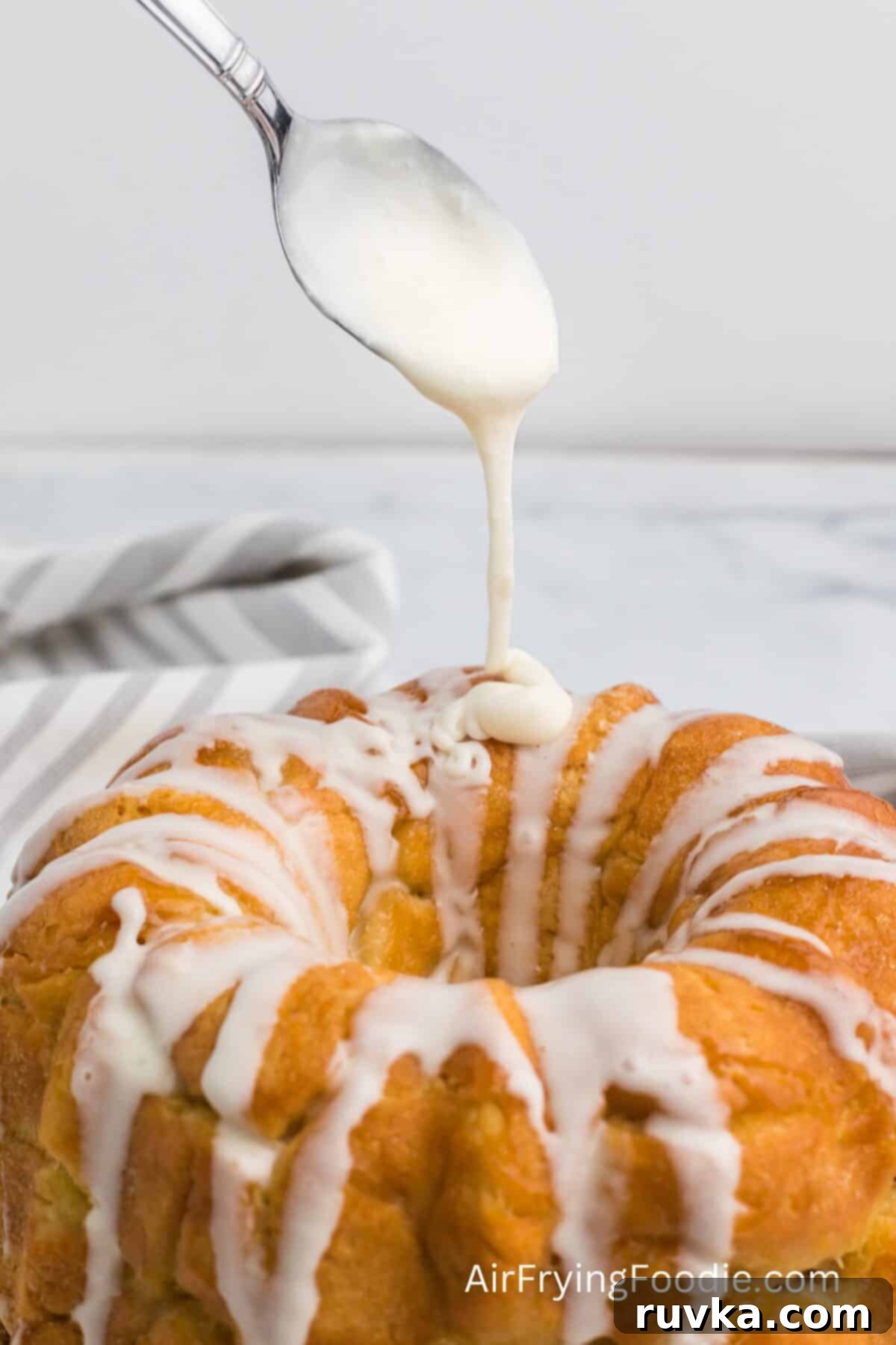 Air-Fried Gooey Cinnamon Pull-Apart 3 Air fried monkey bread with a spoon drizzling a sugar glaze on top before serving.