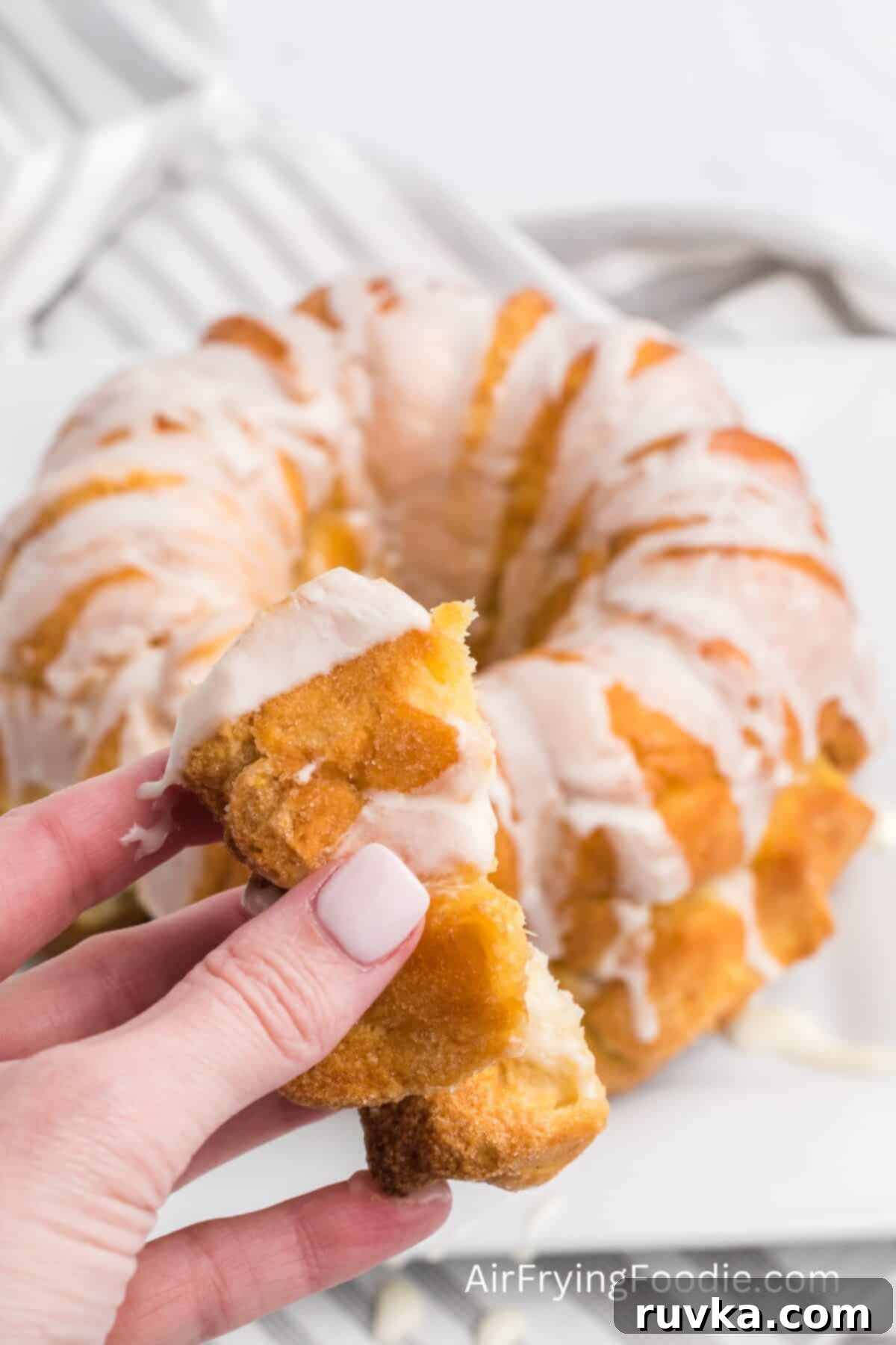 Air-Fried Gooey Cinnamon Pull-Apart 9 hand holding a piece of air fried monkey bread, with the monkey bread in the background.