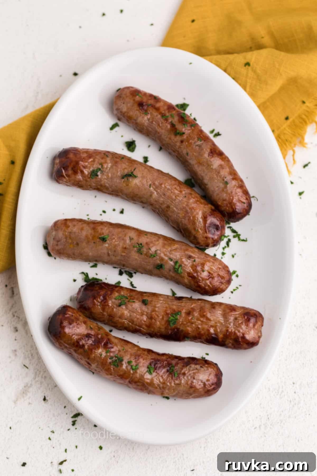 Crispy Air Fryer Italian Sausage 2 Air fried Italian sausage on a white plate garnished with parsley flakes, ready to serve.