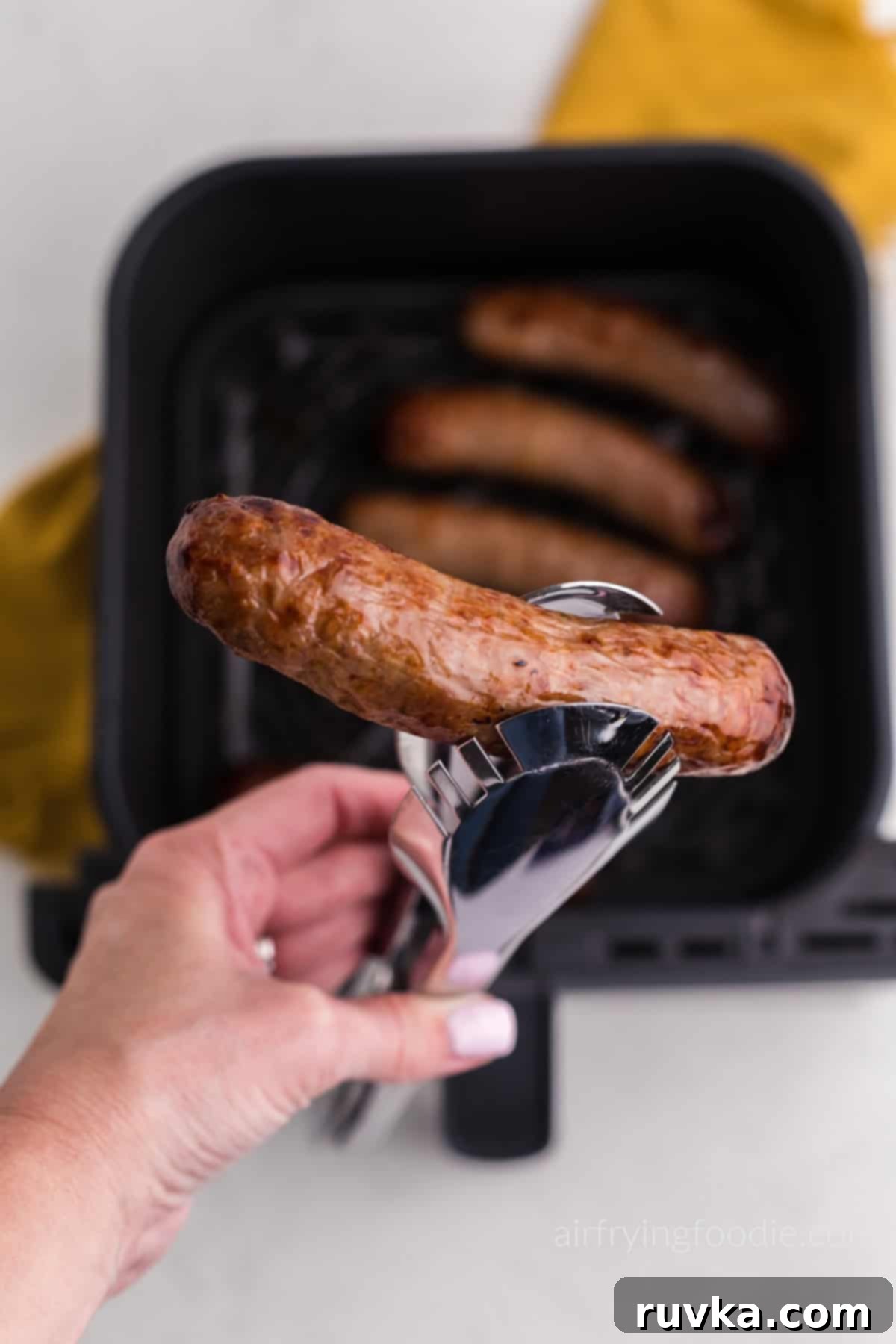 Crispy Air Fryer Italian Sausage 7 Juicy air fried Italian sausage in tongs, ready to serve.