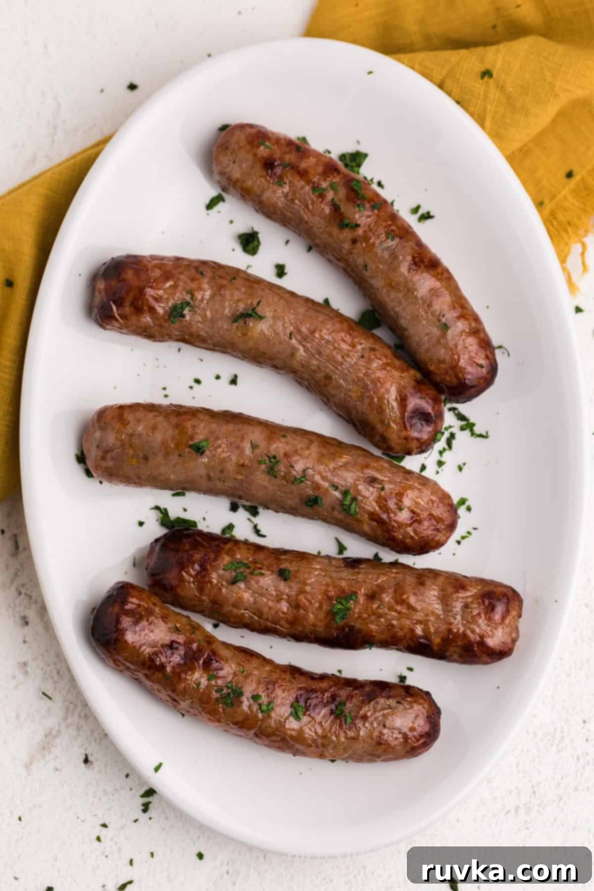 Crispy Air Fryer Italian Sausage 8 Close up of air fryer Italian sausage on a white serving platter garnished with parsley. Ready to serve.