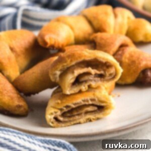 Quick Air Fryer Cinnamon Crescent Rolls 9 Golden filled crescent rolls on a white plate showing one cut in half with cinnamon mixture in the center
