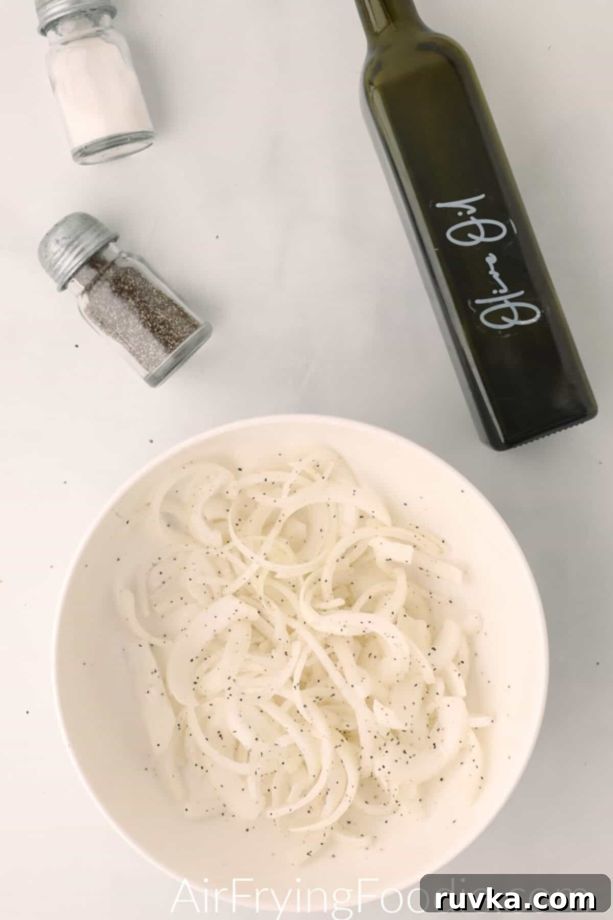 Crispy Air-Fried Onions 5 Onions sliced, in a bowl, and topped with salt, pepper, and olive oil.