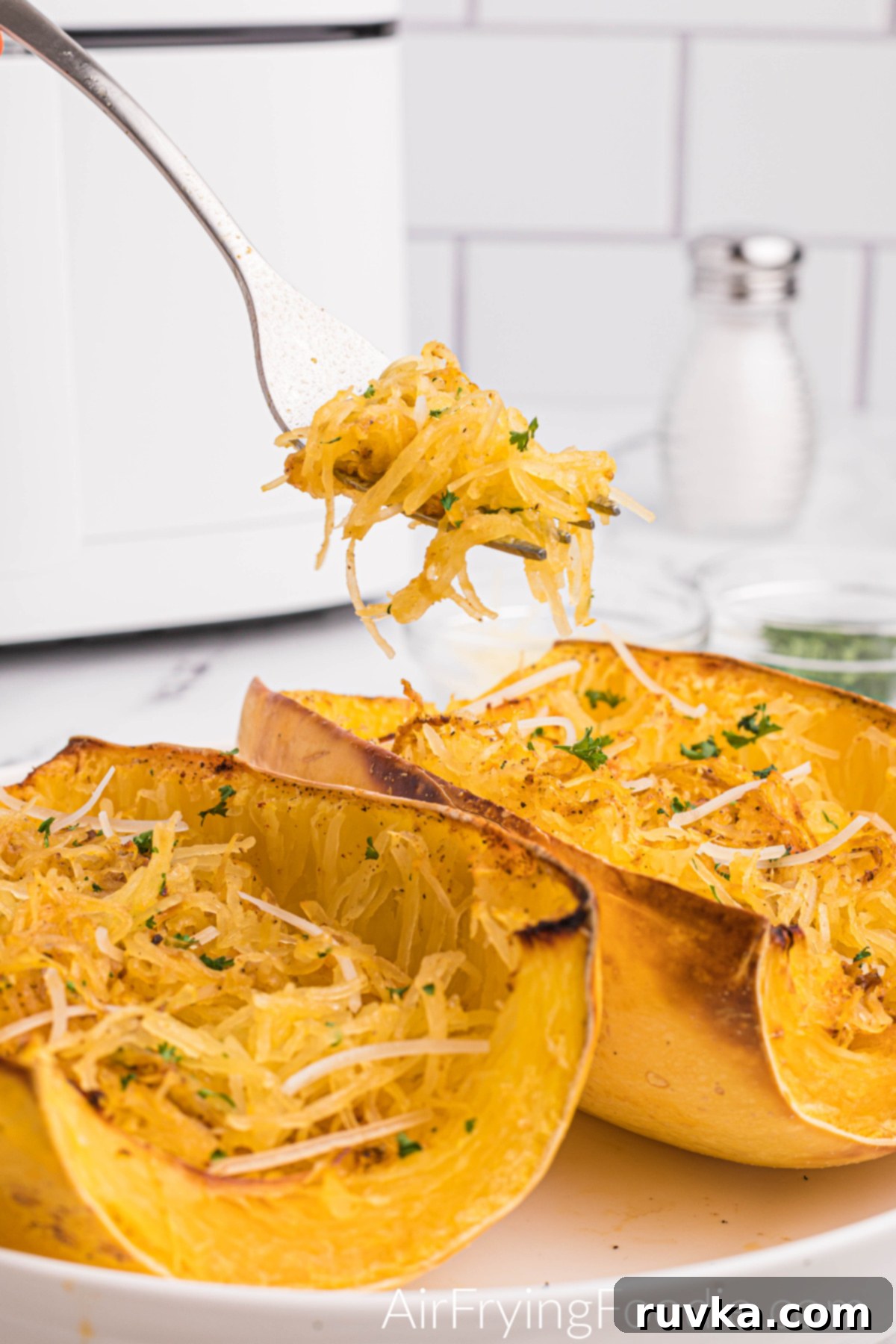 Perfect Air Fryer Spaghetti Squash 2 Spaghetti Squash made in the air fryer and topped with fresh parsley and parmesan cheese, with a bite on a fork.