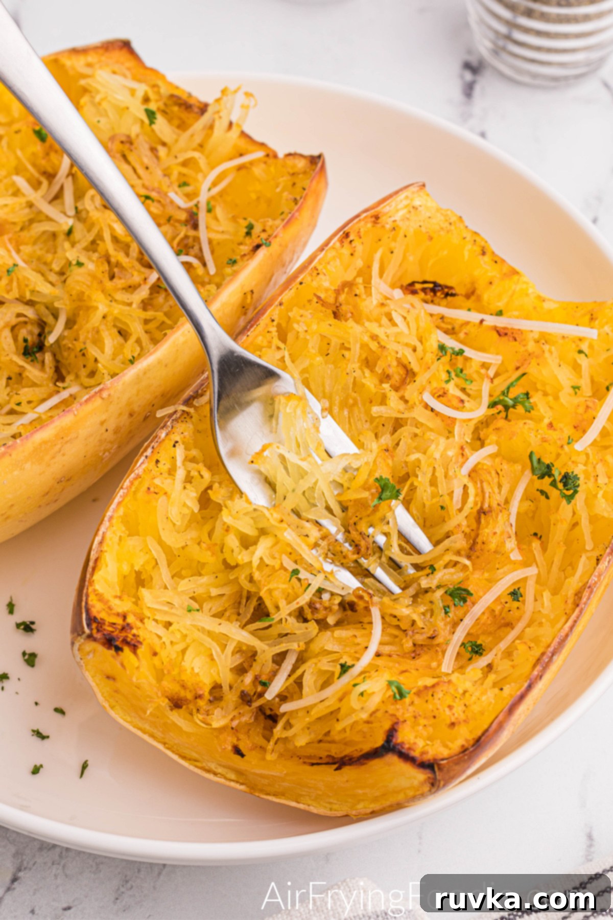 Perfect Air Fryer Spaghetti Squash 3 Spaghetti Squash on a white plate, with parmesan cheese and fresh parsley on top.