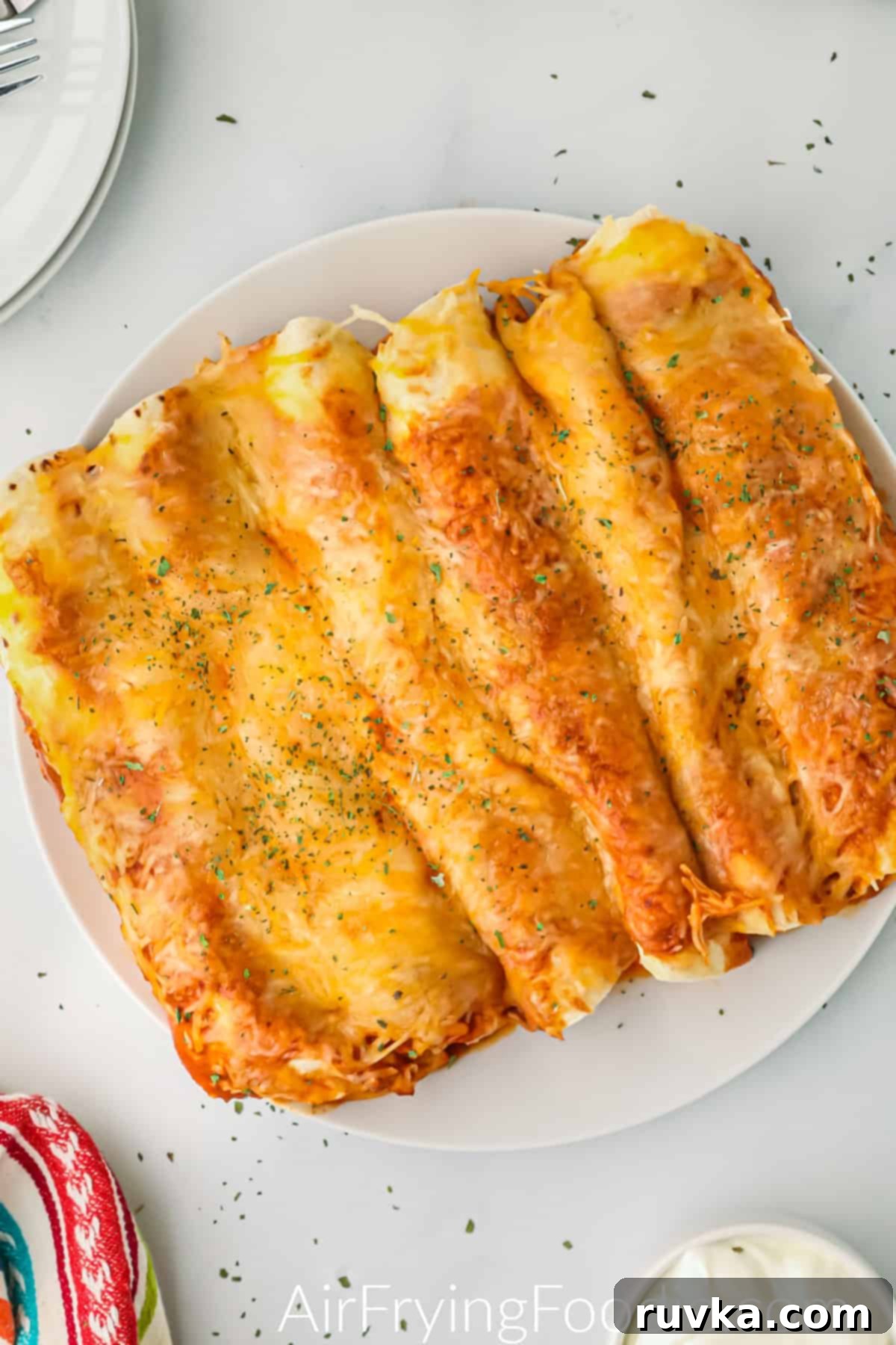 Easy Air Fryer Enchiladas 2 Enchiladas made in the air fryer, served on a white plate and ready to eat.