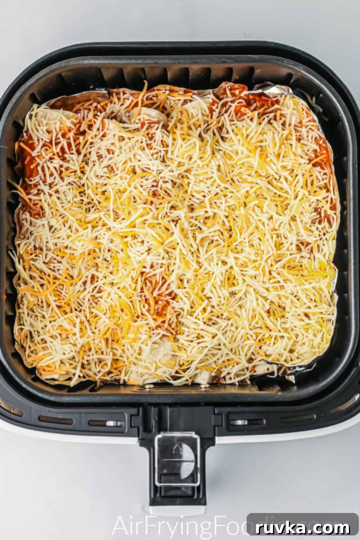 Easy Air Fryer Enchiladas 7 Enchiladas topped with cheese and sauce in the air fryer basket.