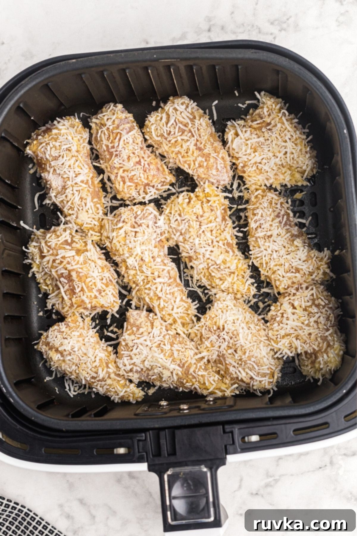 Crispy Air Fryer Coconut Chicken 6 coconut crusted chicken pieces placed in the air fryer basket before being cooked