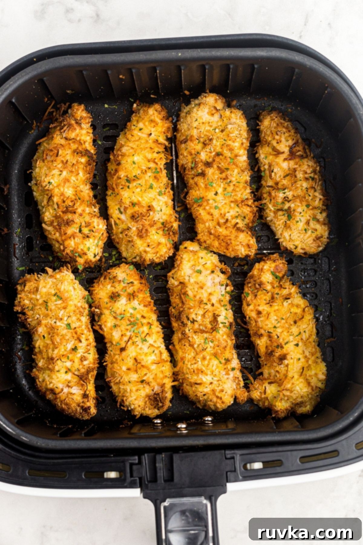 Crispy Air Fryer Coconut Chicken 7 Golden crispy chicken coated with coconut flakes and parsley in the air fryer basket