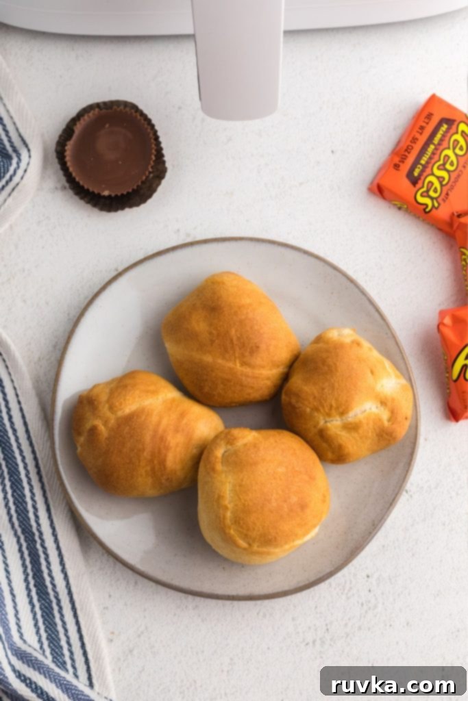 Crispy Air Fryer Peanut Butter Cups 7 Golden pastries on a white plate with reese's peanut butter cups scattered on the table.