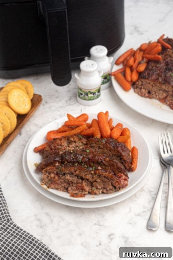 Easy Air Fryer Copycat Cracker Barrel Meatloaf 6 Cooked and sliced meatloaf on a white plate with baby carrots, in front of an air fryer.