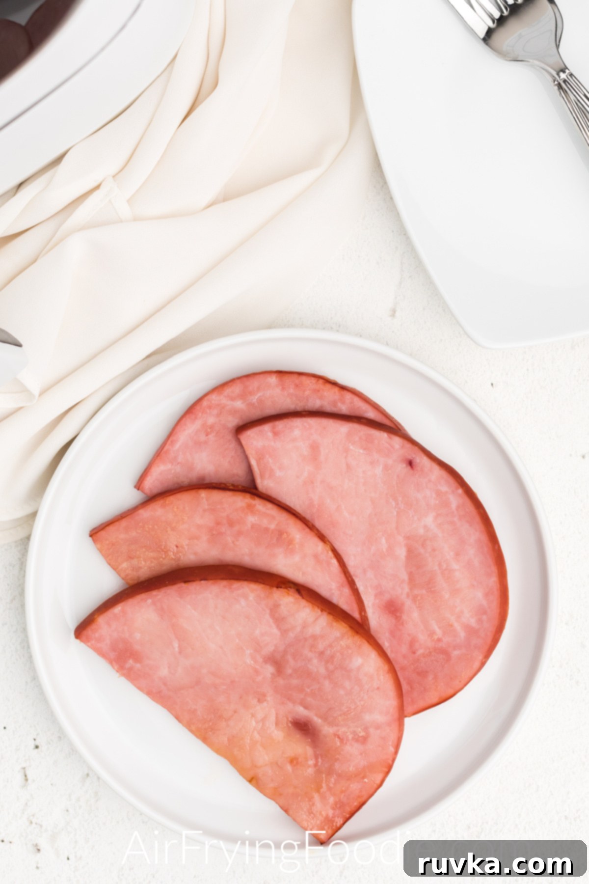 Easy Air Fryer Ham Steak 5 Air fried ham steaks fully cooked and served on a white plate.
