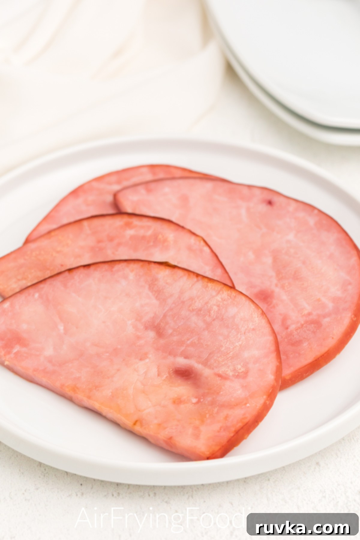 Easy Air Fryer Ham Steak 6 Air fried ham steaks on a white plate ready to serve.