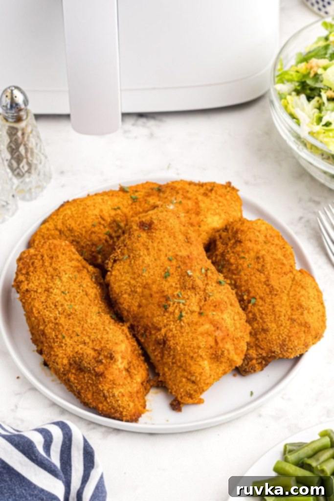 Perfectly Crispy Air Fryer Shake and Bake Chicken 8 Crispy coated chicken breasts on a white plate with green beans and salad on the table