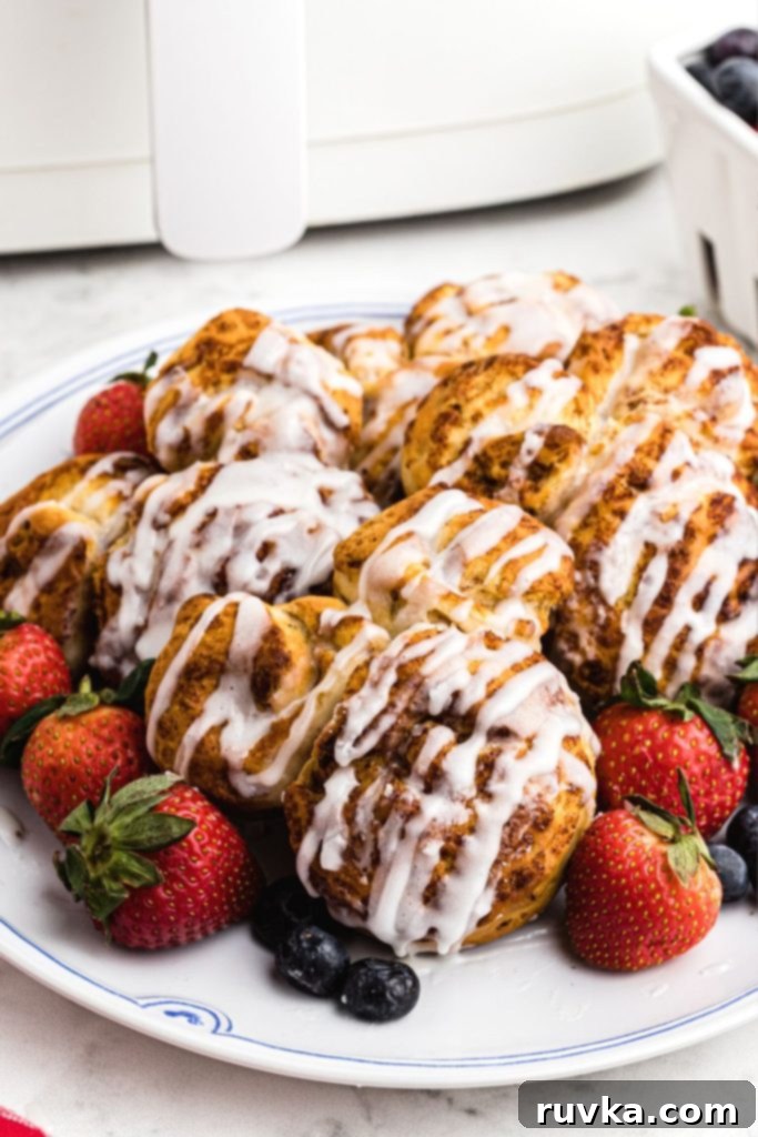 Mickey's Air Fryer Cinnamon Rolls 2 Adorable golden-brown Mickey Mouse shaped cinnamon rolls on a white plate, garnished with fresh blueberries and strawberries.