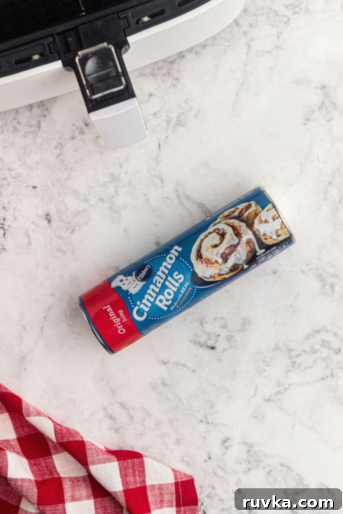 Mickey's Air Fryer Cinnamon Rolls 3 A can of refrigerated cinnamon roll dough on a white marble countertop, with an air fryer basket in the background, ready for use.
