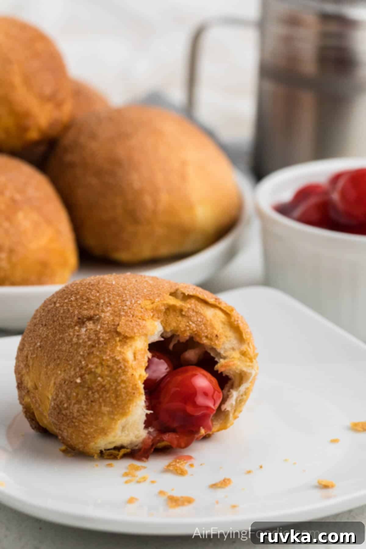 Air Fryer Cherry Pie Bites 2 Cherry pie bombs on a plate in the background, and a cherry pie bombs on a plate with a bite missing in the foreground.