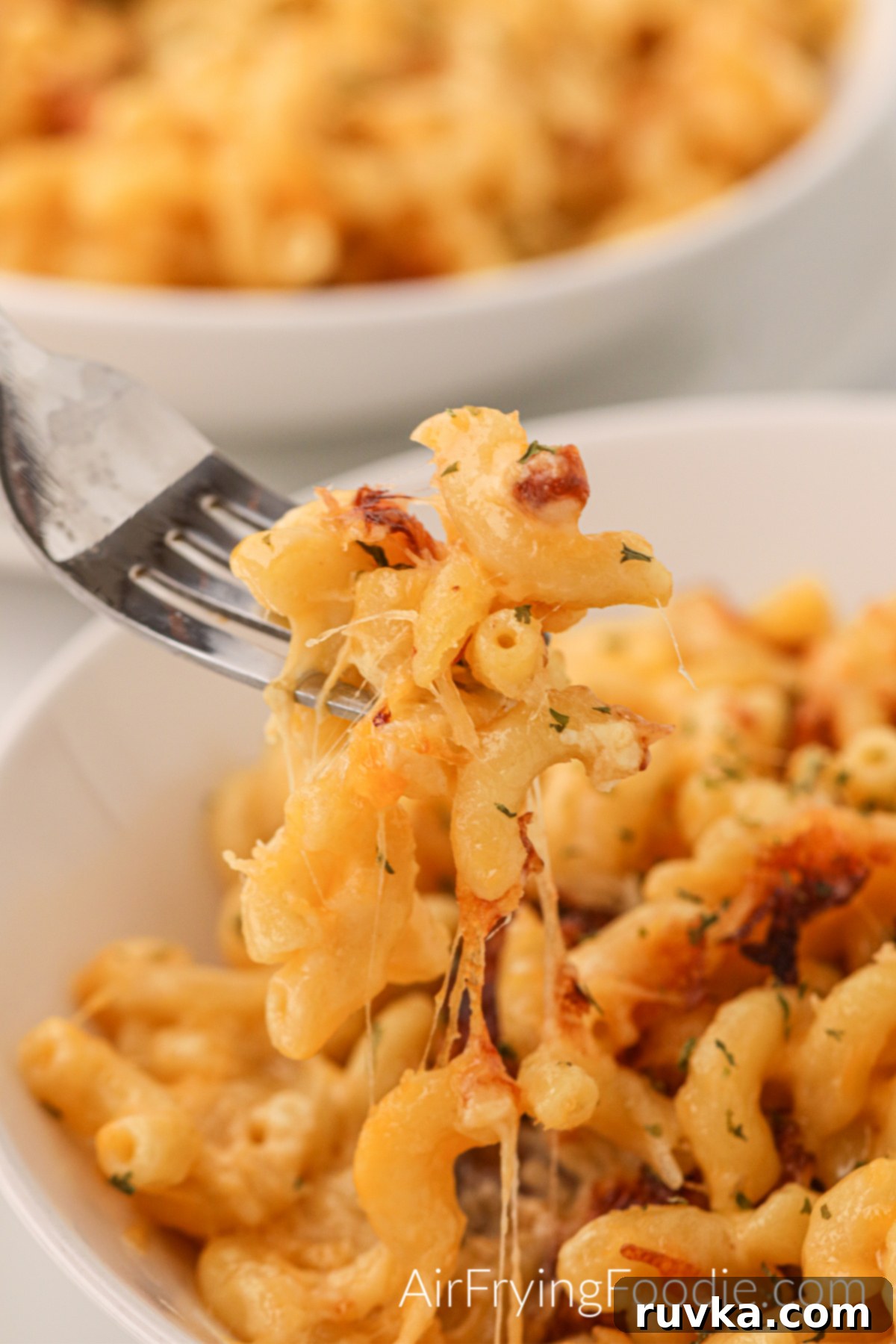 Crispy Air Fryer Mac and Cheese 9 Bite of mac and cheese on a fork with mac and cheese in a bowl.