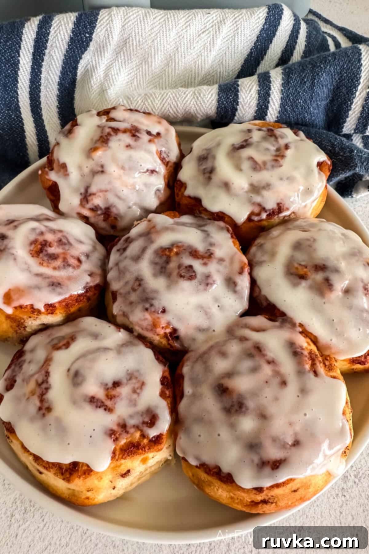 Air-Fried Cinnamon Rolls 2 Cinnamon rolls made in the air fryer and served on a white plate, showcasing their golden brown tops and gooey centers.