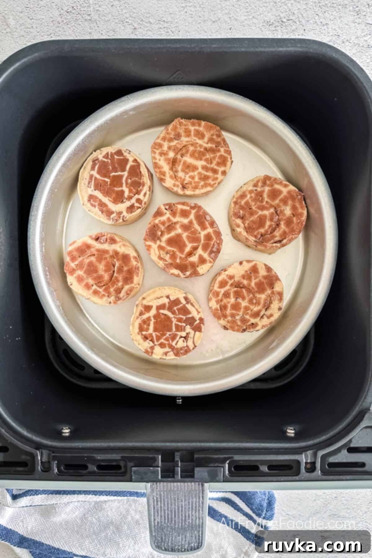 Air-Fried Cinnamon Rolls 4 Cinnamon rolls placed in a prepared pan and inserted into the air fryer basket, ready to be cooked.