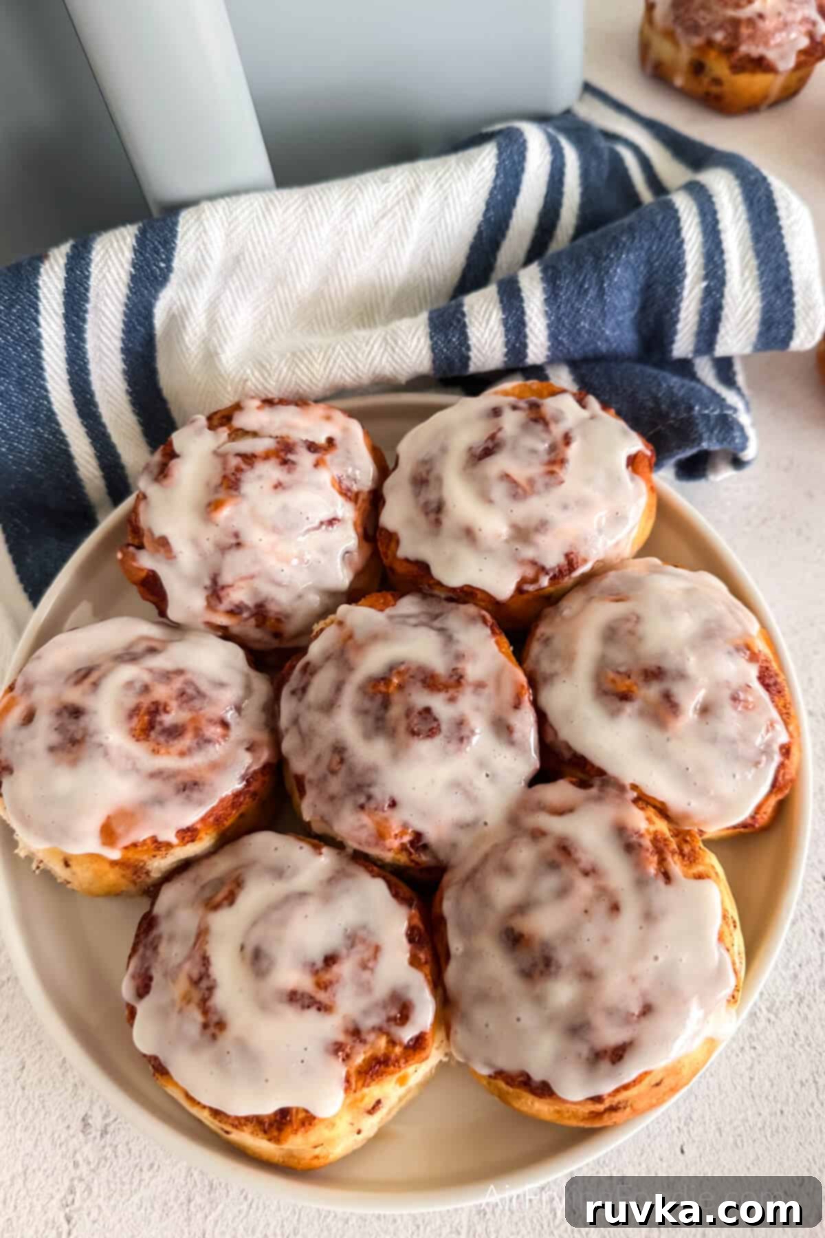 Air-Fried Cinnamon Rolls 6 Cinnamon rolls topped with generous frosting and ready to be served on a white plate.