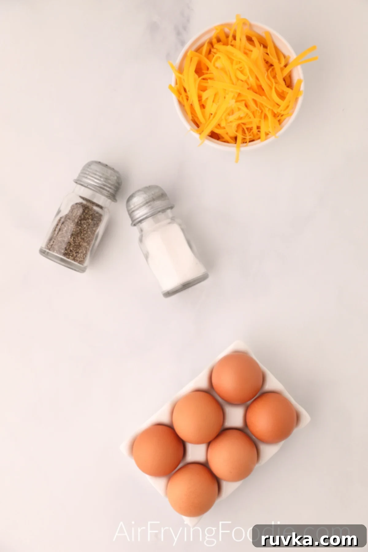 Fluffy Air Fryer Scrambled Eggs 3 Ingredients needed to make scrambled eggs in the air fryer - cheese in a bowl, salt and pepper, and eggs.