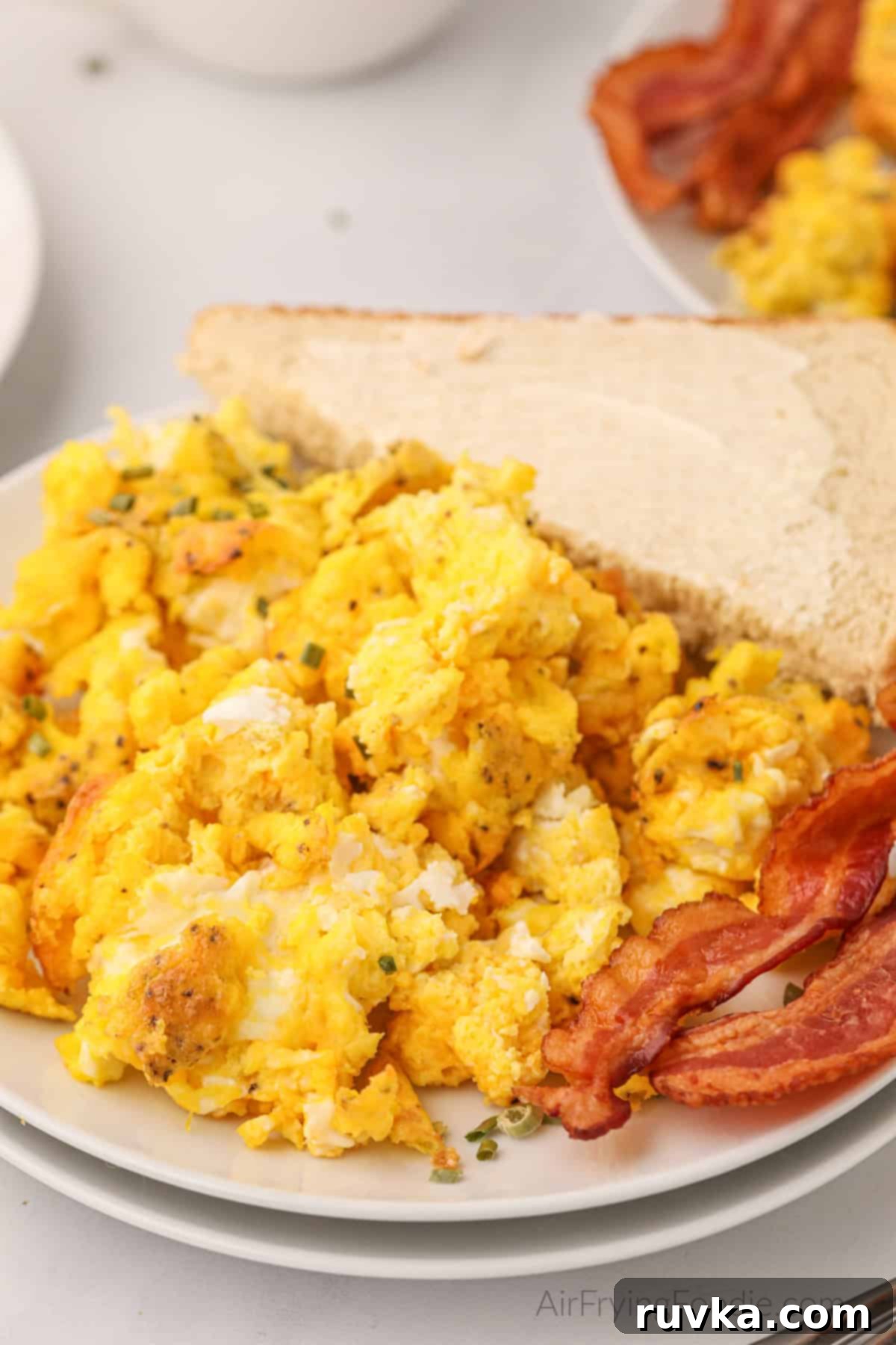 Fluffy Air Fryer Scrambled Eggs 7 Fluffy air fryer scrambled eggs on a plate with bacon and a side of buttered bread.