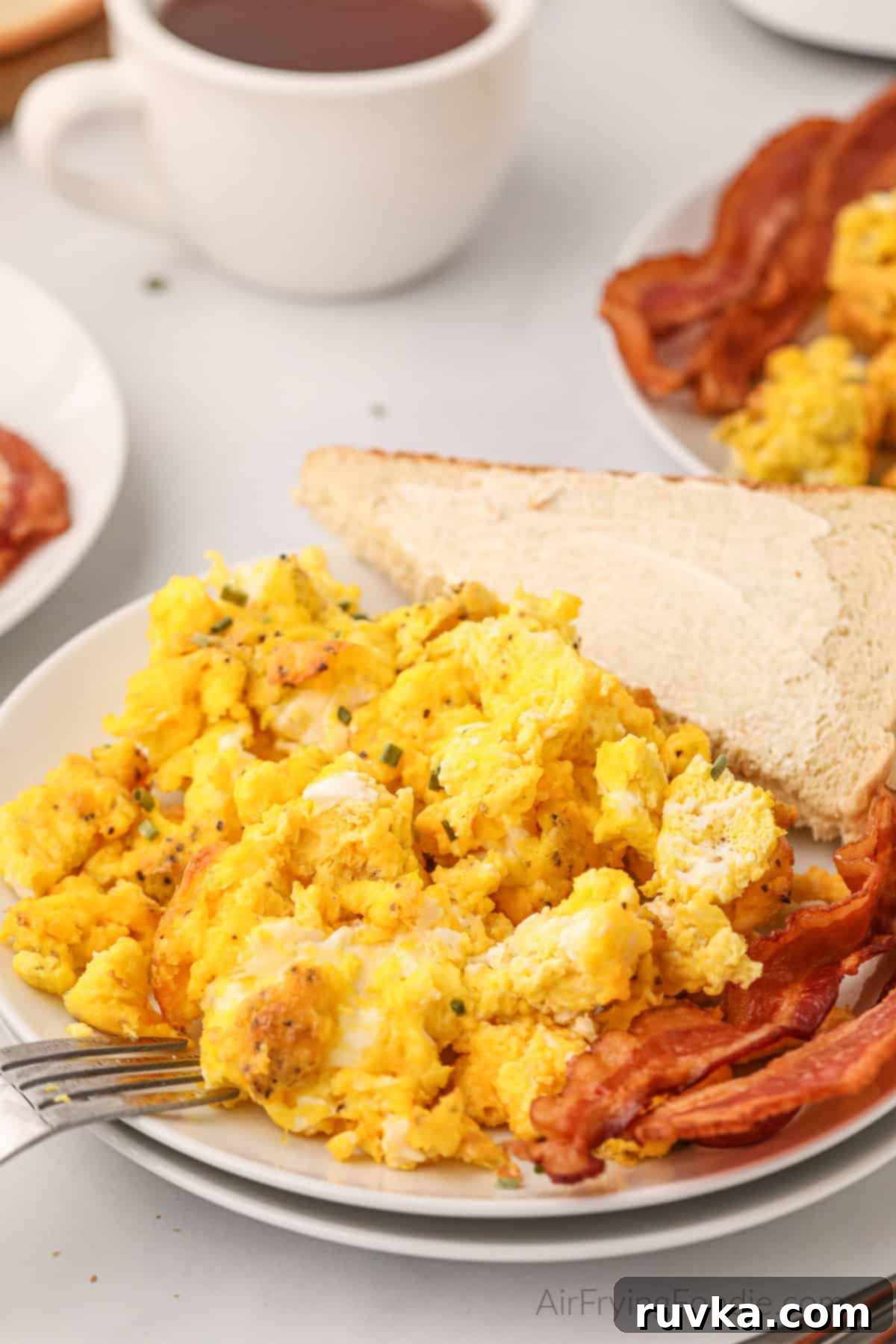 Fluffy Air Fryer Scrambled Eggs 8 Air fried scrambled eggs on a plate with bacon and a side of buttered bread.
