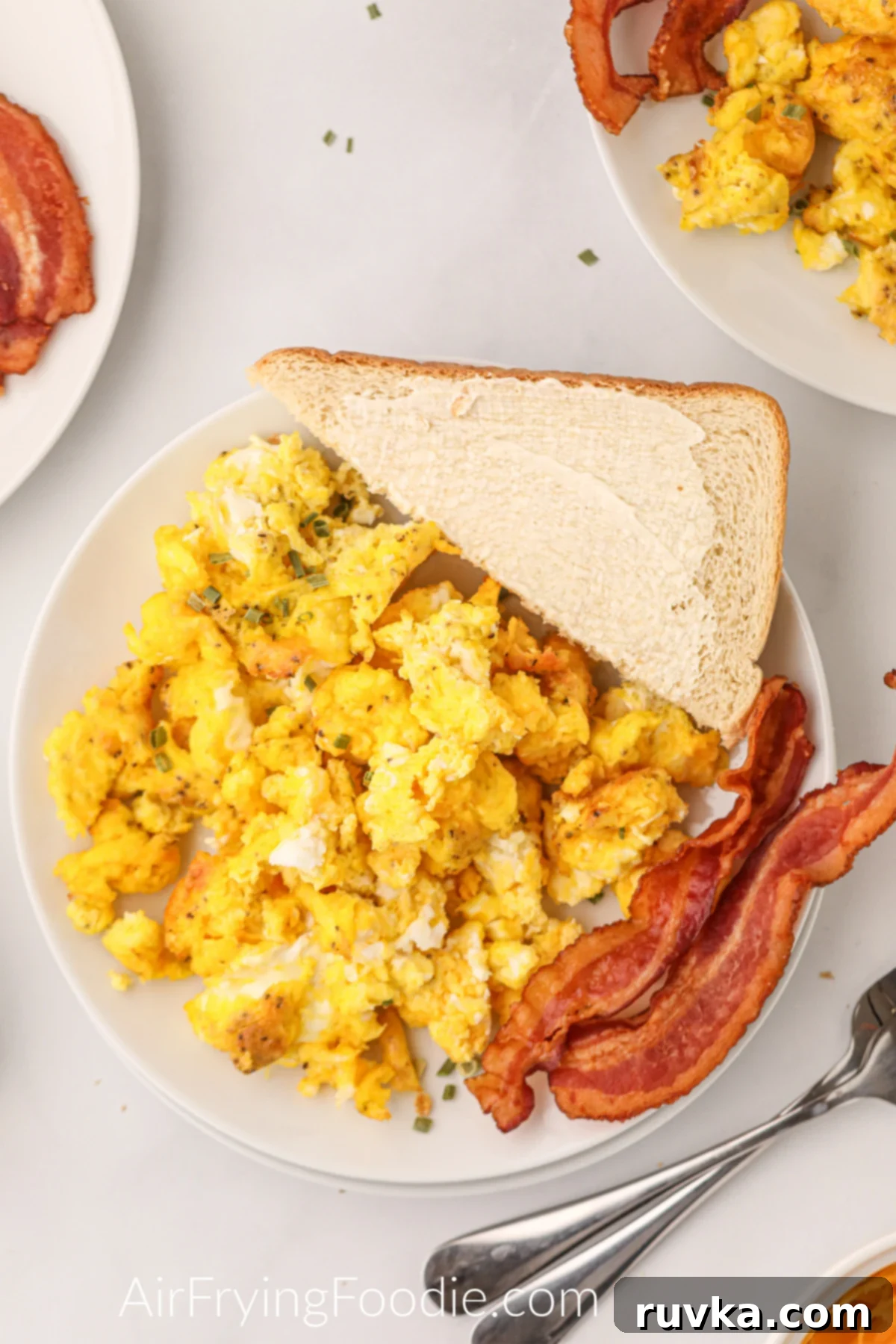 Fluffy Air Fryer Scrambled Eggs 9 Air Fryer Scrambled eggs on a plate with toast and bacon and ready to eat.