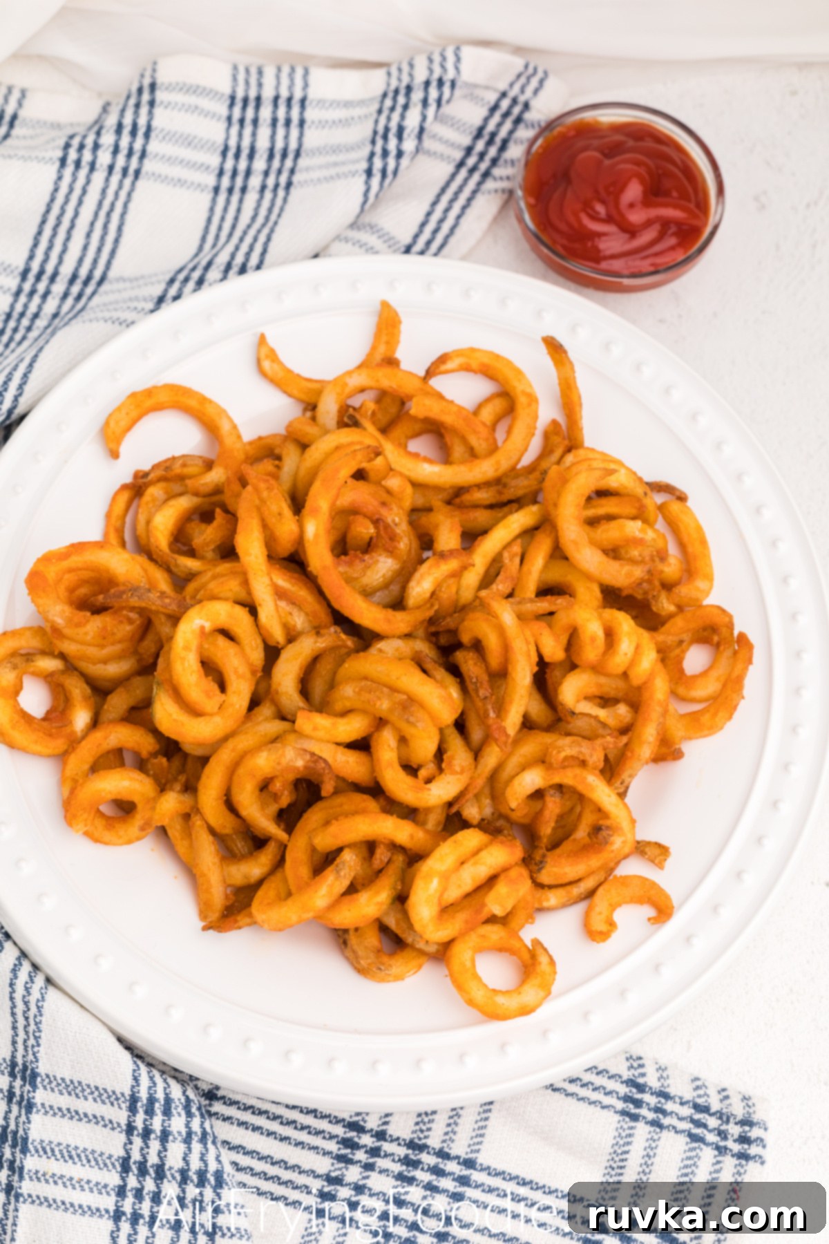 Crispy Air Fryer Frozen Curly Fries 2 air fried curly fries on a white plate ready to eat.