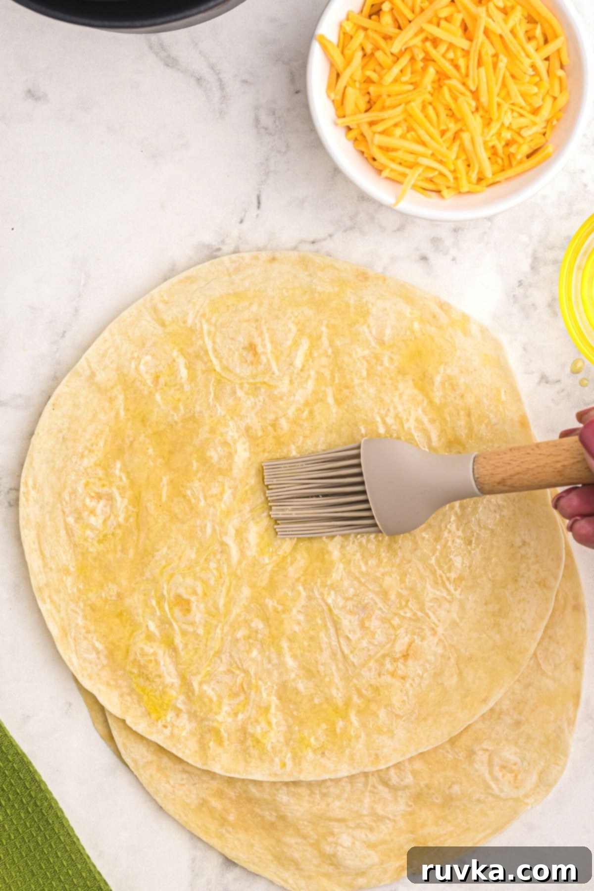 Crispy Air Fryer Quesadillas 4 A hand expertly brushing olive oil onto a flour tortilla, meticulously preparing it for the air fryer to achieve optimal crispiness.