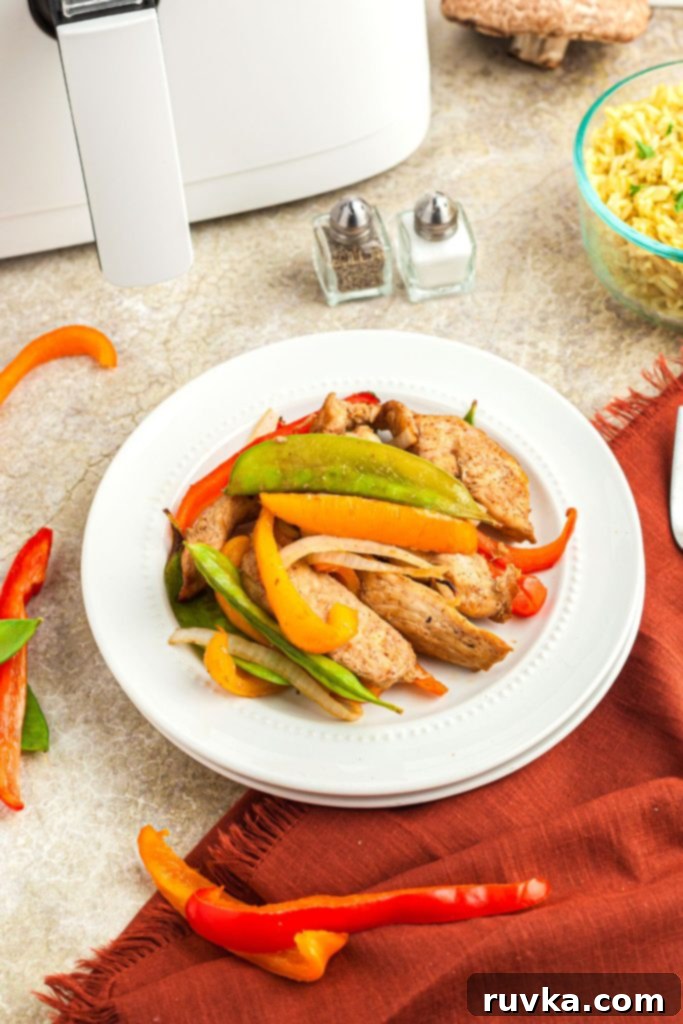 Crispy Air Fryer Stir-Fry 2 Chicken stir fry with peppers and mushrooms on a white plate in front of an air fryer and salt and pepper shakers.
