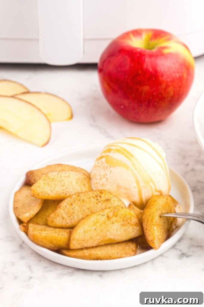 Perfect Air Fryer Apples 2 Golden juicy air fryer apples served on a white plate with a scoop of creamy caramel ice cream, placed on a elegant marble table, ready to be enjoyed.
