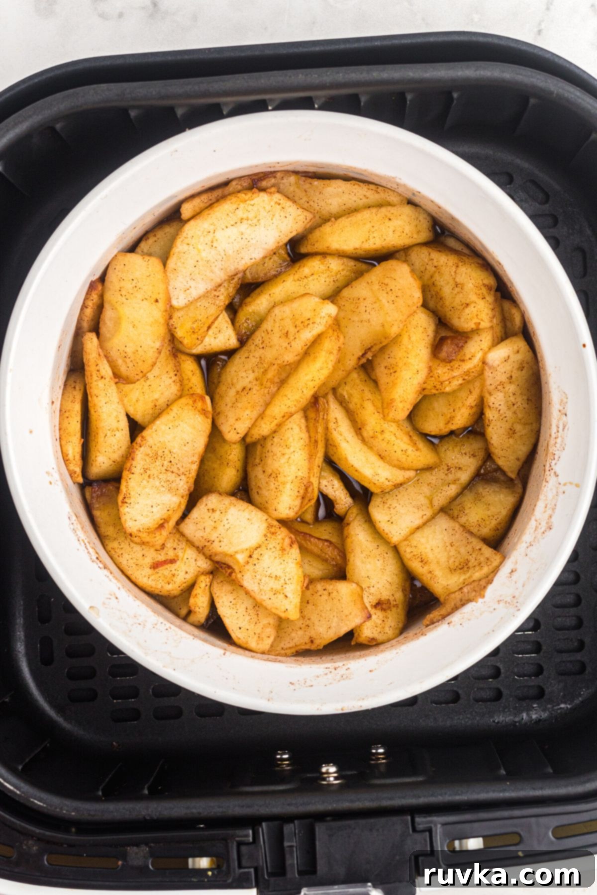 Perfect Air Fryer Apples 6 Perfectly air-fried golden and juicy apple slices, now tender and caramelized, presented in a white bowl directly from the air fryer basket, steam gently rising, showcasing their delicious readiness.