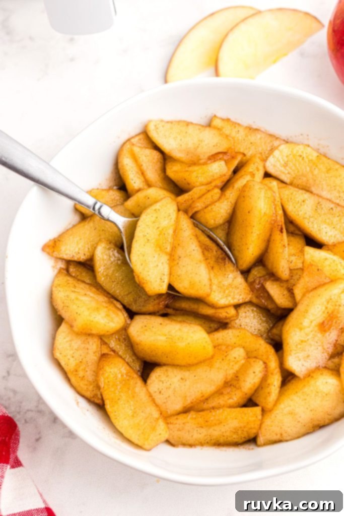 Perfect Air Fryer Apples 7 A close-up of golden, juicy air-fried apple slices served in a rustic white bowl, with a spoon gently scooping a portion, highlighting their tender texture and inviting aroma.