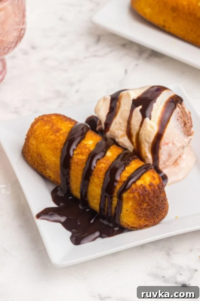 Warm Golden Air Fryer Twinkies 2 Golden crispy Air Fryer Twinkie drizzled with rich chocolate sauce, served elegantly with a scoop of creamy vanilla ice cream on a white plate.