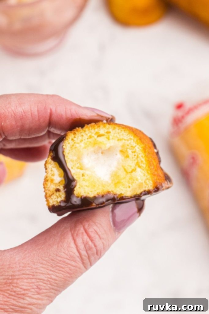 Warm Golden Air Fryer Twinkies 8 A hand holding half of a warm, air-fried Twinkie, revealing its creamy filling, with luscious chocolate sauce drizzled generously over it.