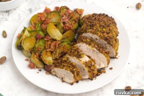 Crispy Pistachio Air Fryer Chicken 2 Pistachio crusted chicken cut into slices, served on a white plate next to Brussel sprouts.